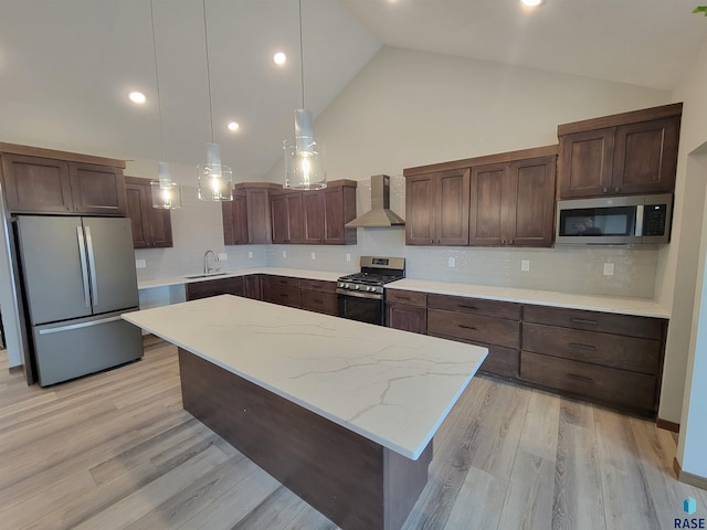 kitchen featuring appliances with stainless steel finishes, a sink, wall chimney range hood, and light wood-style flooring