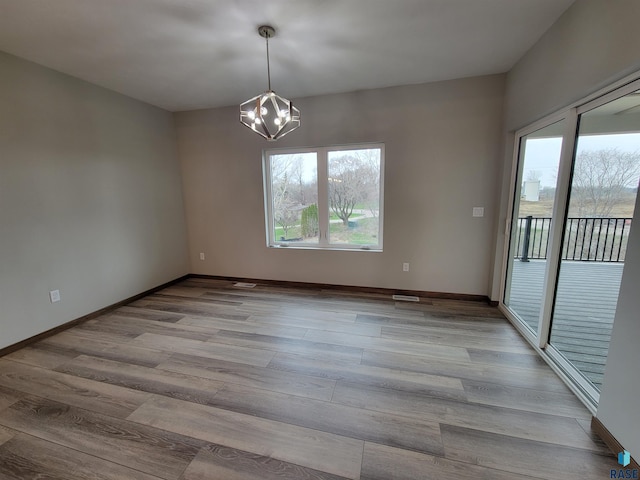 unfurnished room with a healthy amount of sunlight, a chandelier, and wood finished floors