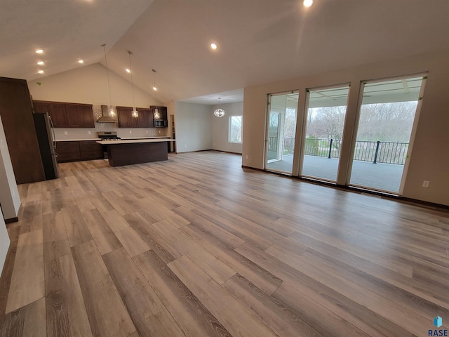 unfurnished living room featuring high vaulted ceiling, recessed lighting, baseboards, light wood-style floors, and an inviting chandelier