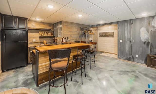 bar with black fridge, concrete flooring, and wooden walls