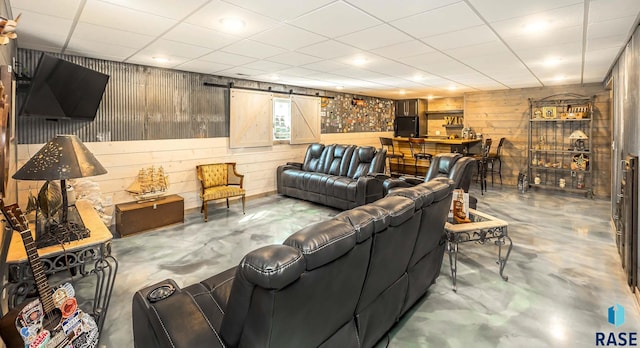 living room with a paneled ceiling, concrete flooring, a barn door, and wooden walls