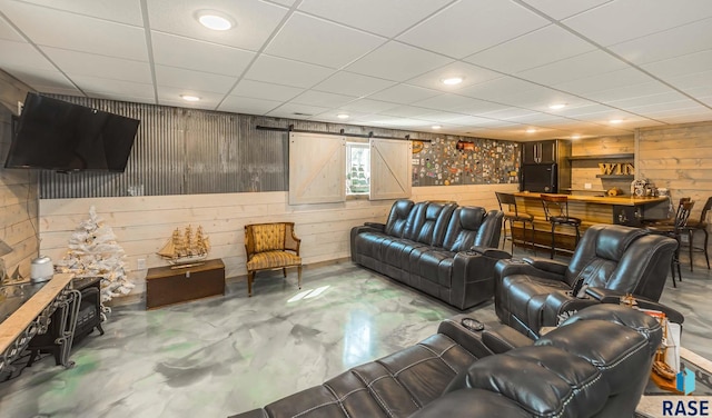 living room with a barn door, concrete floors, wood walls, and a drop ceiling