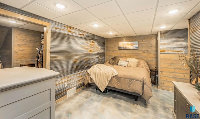 bedroom with concrete floors, wood walls, and a drop ceiling