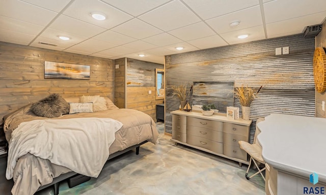 bedroom with a paneled ceiling, wooden walls, and concrete floors