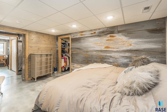 bedroom with wood walls, a spacious closet, concrete floors, a closet, and a paneled ceiling