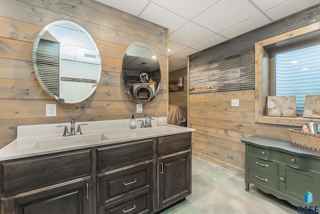 bathroom with vanity, wooden walls, concrete flooring, and a drop ceiling