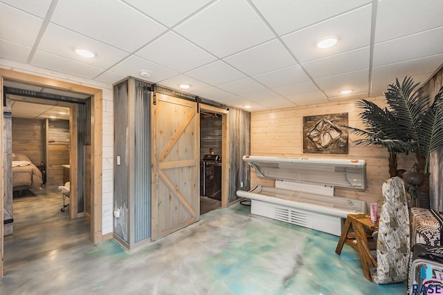 basement featuring a barn door, a paneled ceiling, and wood walls