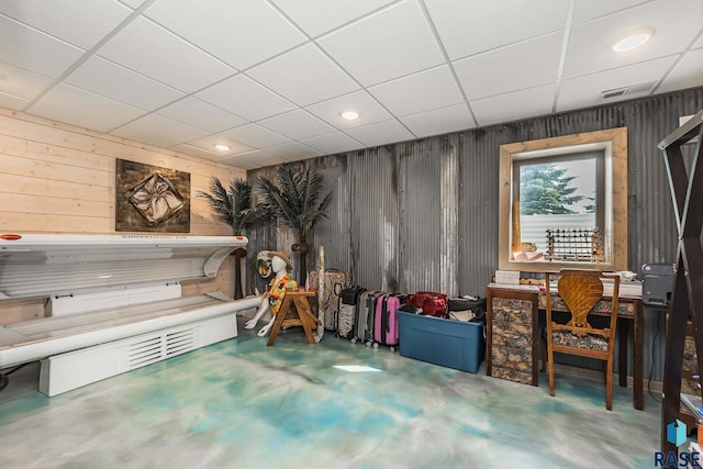 misc room featuring a paneled ceiling, concrete floors, and wood walls