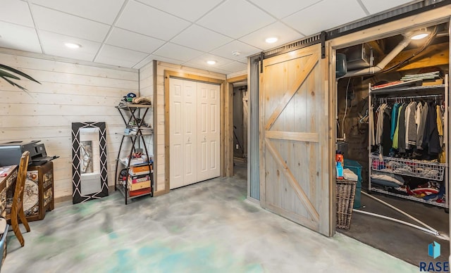 basement featuring a barn door, wood walls, and a drop ceiling