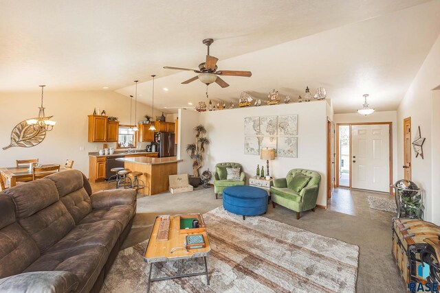 carpeted living room with ceiling fan with notable chandelier, vaulted ceiling, and a wealth of natural light