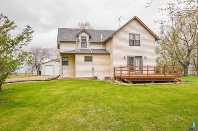 rear view of house featuring an outbuilding, driveway, roof with shingles, a deck, and a lawn