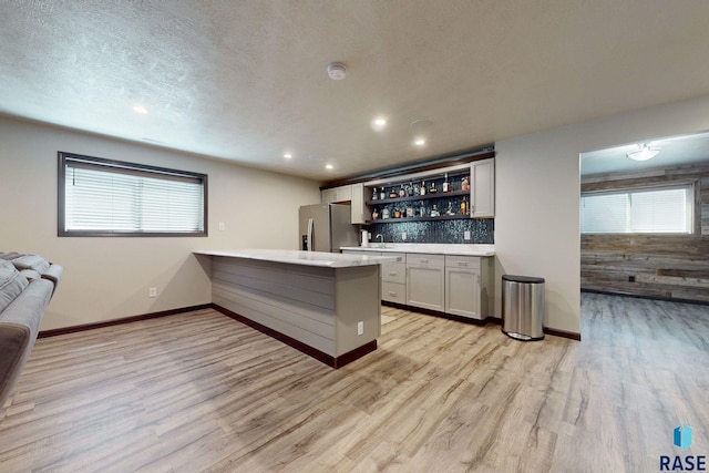 kitchen featuring stainless steel fridge with ice dispenser, light wood-type flooring, a wealth of natural light, and kitchen peninsula