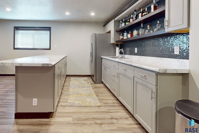 kitchen with backsplash, gray cabinetry, light wood-type flooring, sink, and stainless steel fridge