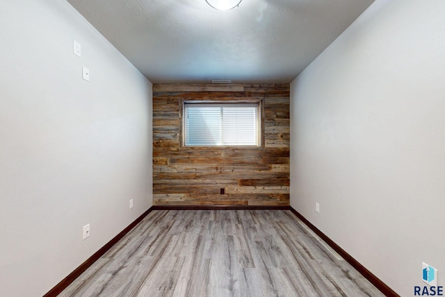 unfurnished room featuring a textured ceiling, wooden walls, and light hardwood / wood-style floors