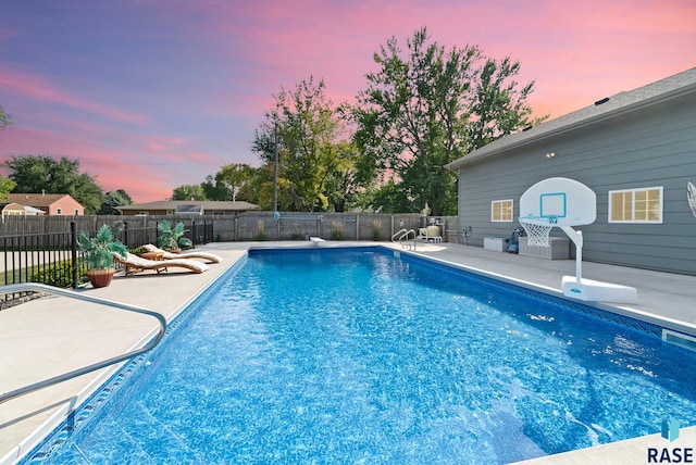 pool at dusk featuring a diving board and a patio