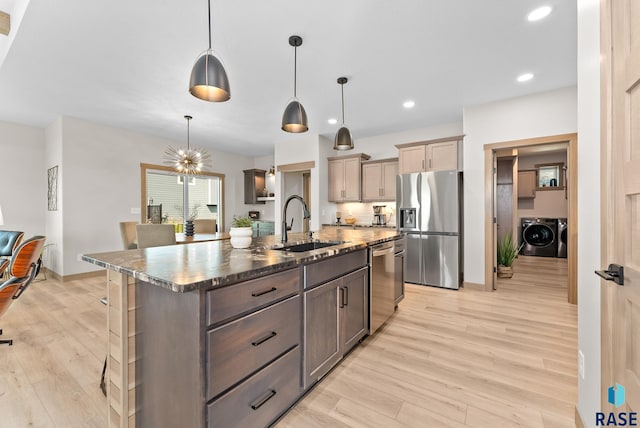 kitchen featuring light wood-type flooring, washing machine and dryer, an island with sink, sink, and appliances with stainless steel finishes