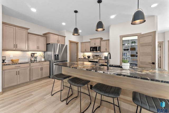 kitchen featuring dark stone counters, light hardwood / wood-style flooring, hanging light fixtures, appliances with stainless steel finishes, and a breakfast bar area