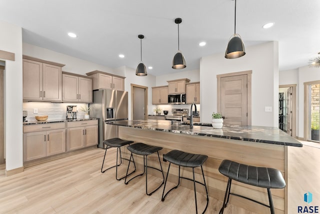 kitchen with a kitchen island with sink, light hardwood / wood-style flooring, a kitchen bar, sink, and appliances with stainless steel finishes