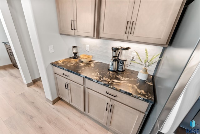 bar featuring light hardwood / wood-style flooring, stainless steel refrigerator, backsplash, and dark stone counters