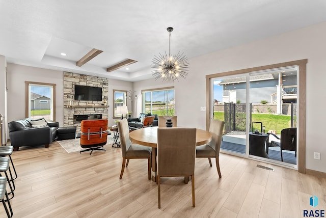 dining room featuring light hardwood / wood-style flooring, an inviting chandelier, a tray ceiling, and a fireplace