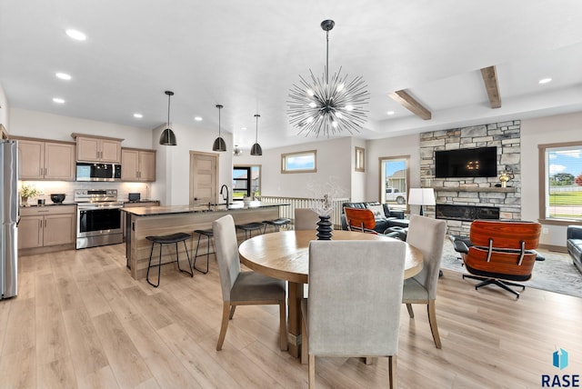 dining room with light wood-type flooring, a notable chandelier, sink, beamed ceiling, and a stone fireplace