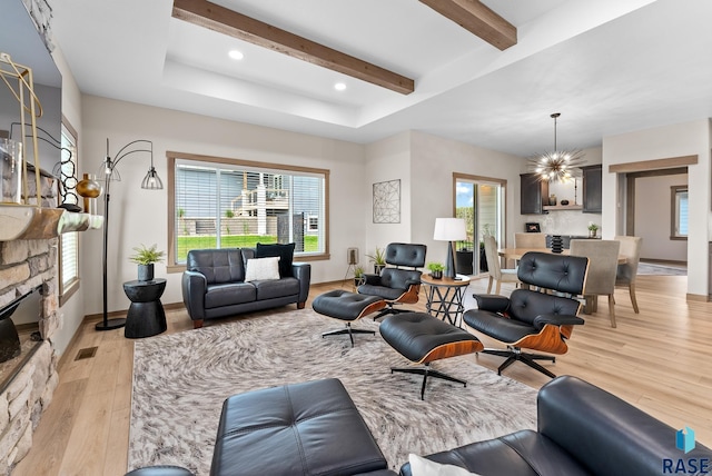 living room featuring an inviting chandelier, a stone fireplace, beam ceiling, and light hardwood / wood-style floors