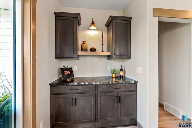 bar featuring dark brown cabinetry, dark stone counters, and light hardwood / wood-style floors