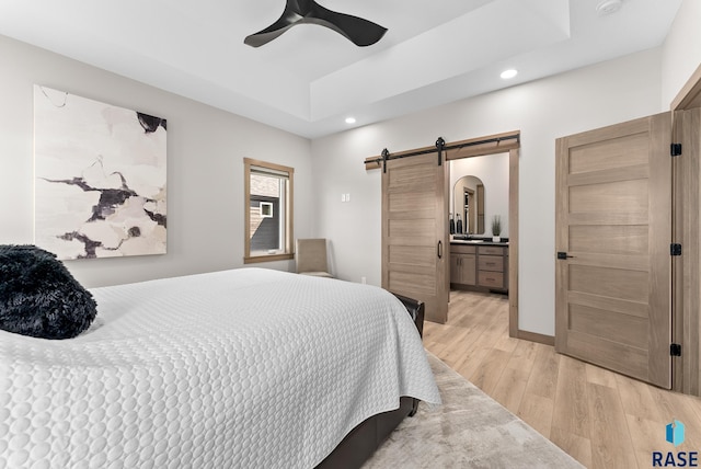 bedroom featuring light wood-type flooring, ceiling fan, ensuite bathroom, and a barn door