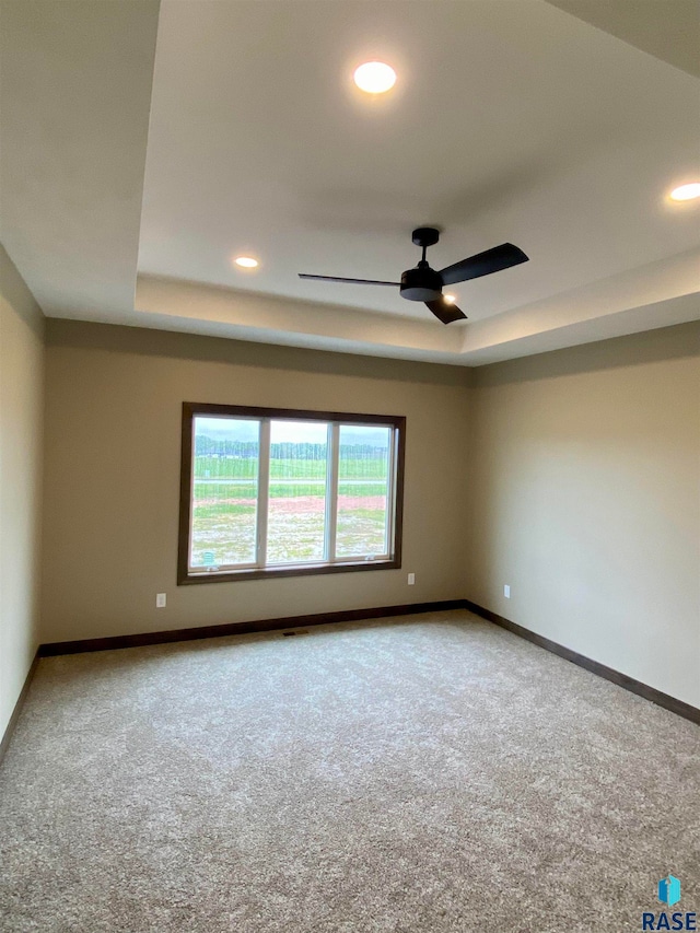 empty room featuring carpet flooring, a tray ceiling, and ceiling fan