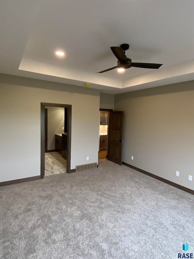 interior space with a tray ceiling, light colored carpet, and ceiling fan