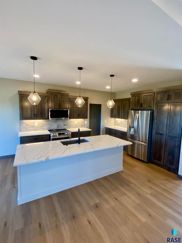 kitchen with appliances with stainless steel finishes, light stone countertops, an island with sink, and sink