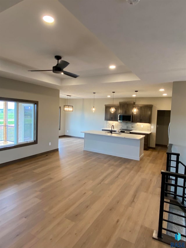 kitchen featuring backsplash, light wood-type flooring, appliances with stainless steel finishes, ceiling fan, and a center island with sink