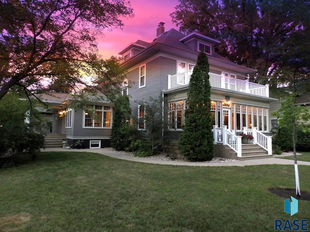 back house at dusk featuring a lawn and a balcony