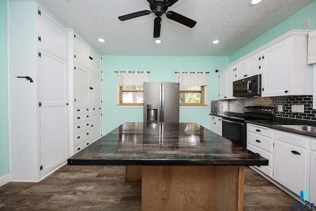 kitchen with dark countertops, a center island, dark wood-style floors, stainless steel fridge, and black electric range oven