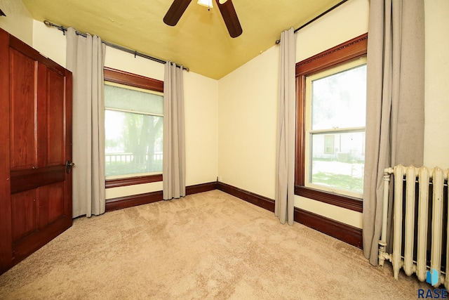 empty room with light colored carpet, a ceiling fan, radiator heating unit, and baseboards