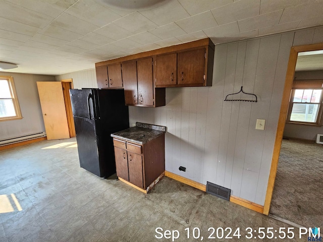 kitchen with wooden walls, a baseboard radiator, light colored carpet, and black fridge