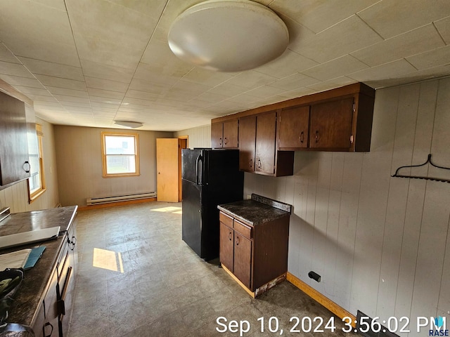 kitchen with a baseboard heating unit, black refrigerator, and wood walls