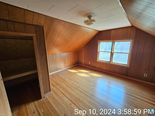 bonus room with lofted ceiling, wood walls, and light hardwood / wood-style flooring