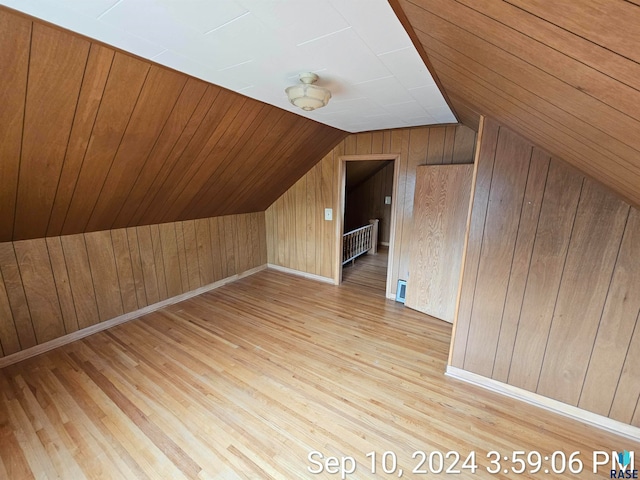 additional living space with radiator heating unit, lofted ceiling, light hardwood / wood-style flooring, and wooden walls