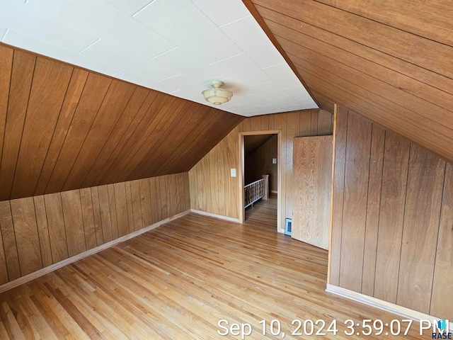 additional living space with vaulted ceiling, wood walls, radiator heating unit, and light wood-type flooring