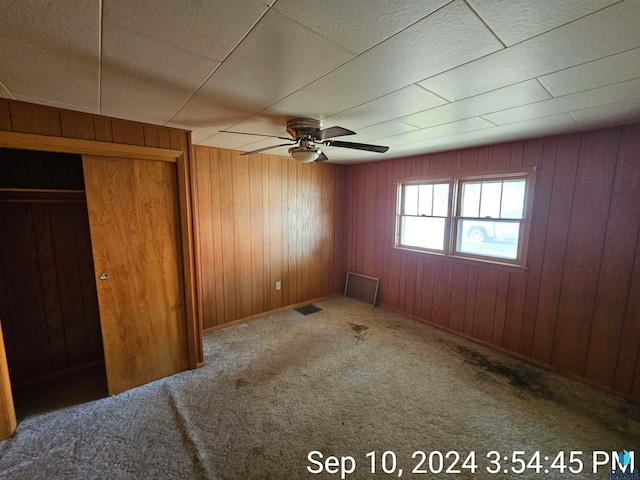 unfurnished bedroom with ceiling fan, wood walls, a closet, and carpet floors