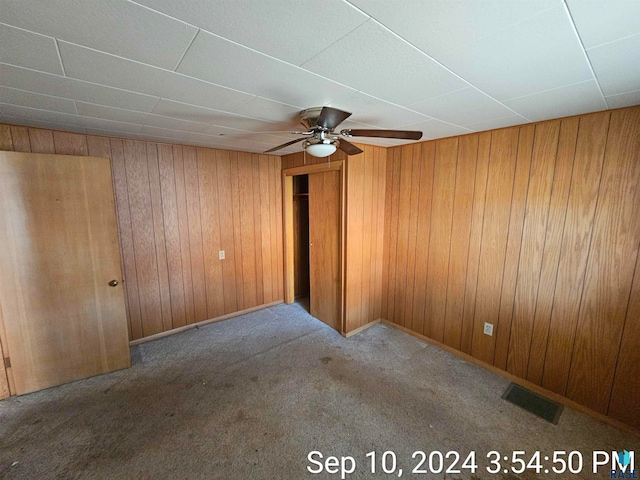 carpeted empty room featuring wood walls and ceiling fan