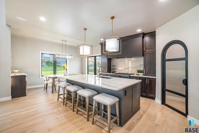 kitchen with light wood-type flooring, a center island with sink, sink, and light stone counters