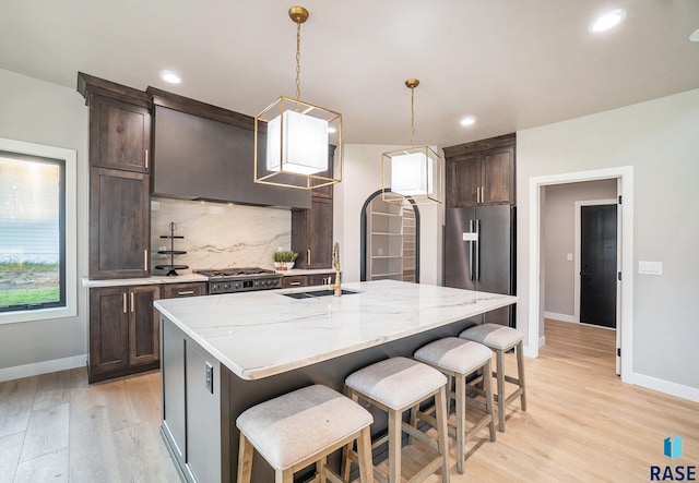 kitchen featuring pendant lighting, light wood-type flooring, a kitchen island with sink, sink, and light stone countertops