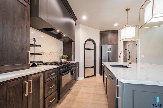 kitchen with light stone counters, sink, tasteful backsplash, stainless steel appliances, and light wood-type flooring