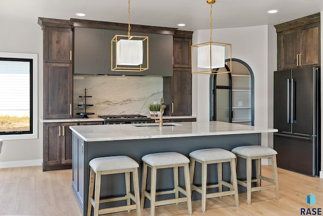 kitchen featuring light stone counters, decorative light fixtures, a center island with sink, light hardwood / wood-style flooring, and appliances with stainless steel finishes