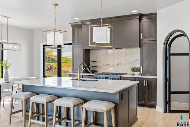 kitchen with decorative light fixtures, an island with sink, light hardwood / wood-style floors, and sink