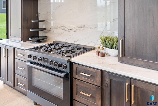 kitchen featuring dark brown cabinetry, backsplash, light stone countertops, and high end stainless steel range oven