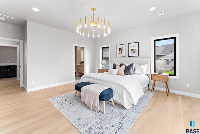 bedroom featuring light hardwood / wood-style flooring, ensuite bathroom, and a chandelier