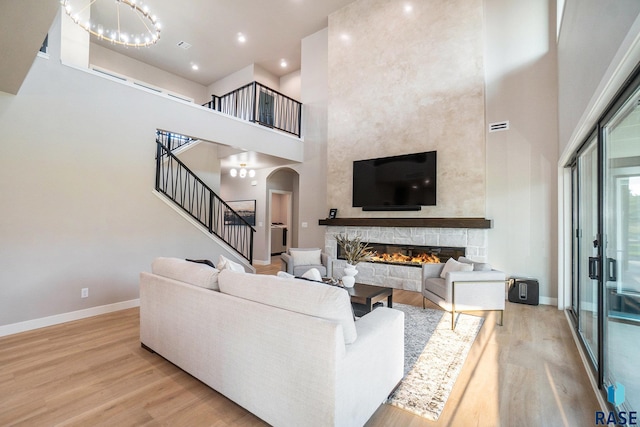 living room with a stone fireplace, light hardwood / wood-style floors, a chandelier, and a high ceiling